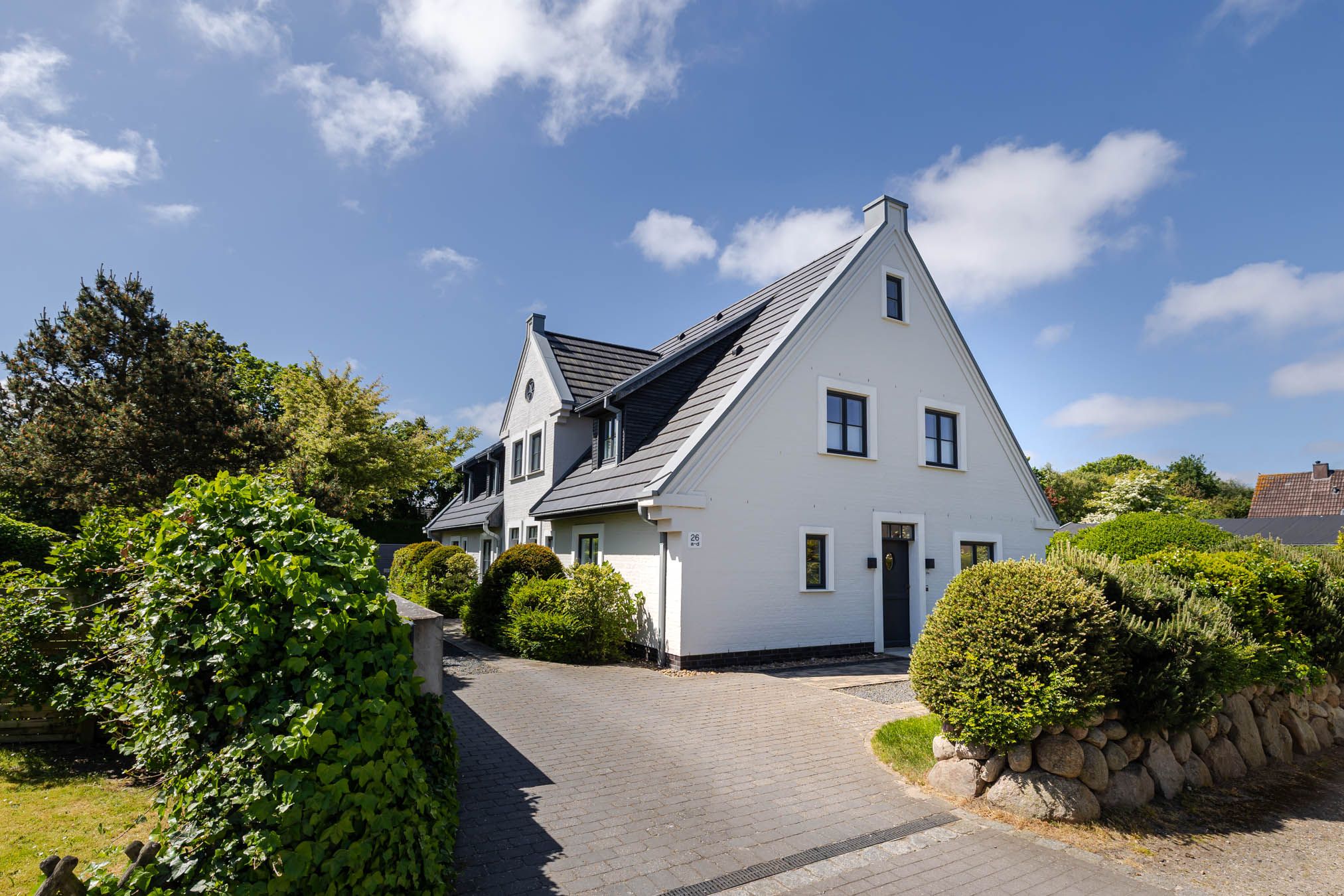 Weißes Friesenhaus mit Hecke in einer ruhigen Straße in Tinnum