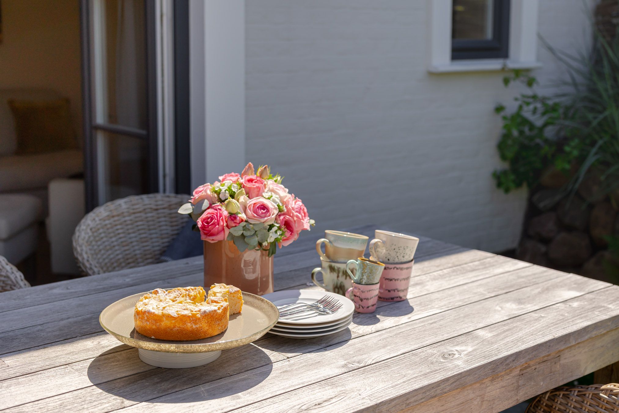 Terrassentisch mit Kuchen und Rosen in der Sonne